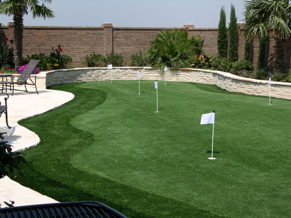 a putting green in a backyard with a brick wall behind it